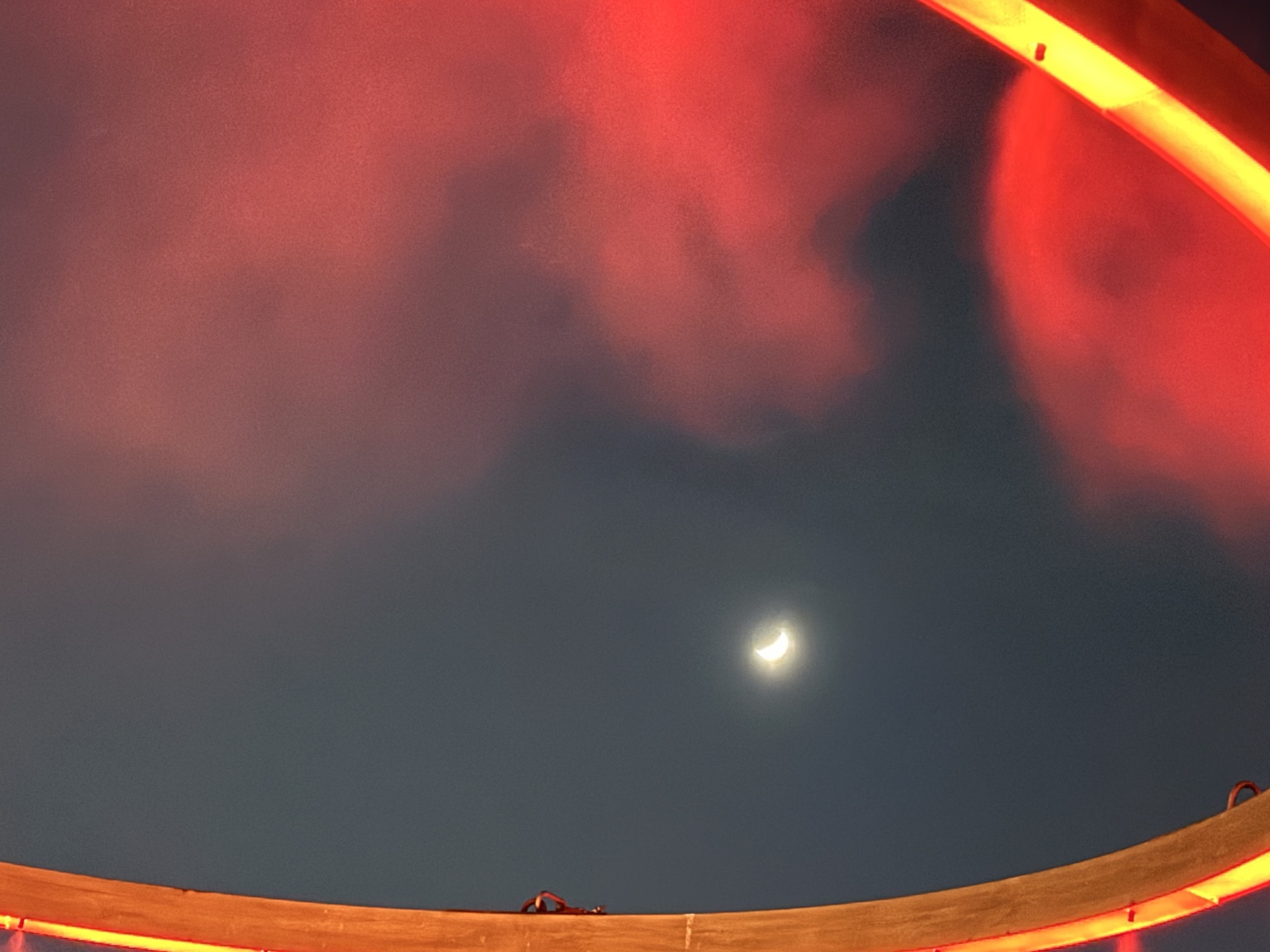 A crescent moon in the night sky framed by warm lights